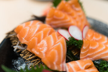 Fresh slices of salmon sashimi are arranged on a black plate. Close up
