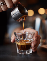 Close-up of barista pouring rich espresso into transparent glass cup