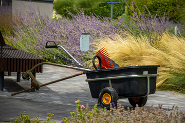 Garden wheelbarrow with tools standing on a path in landscaped park