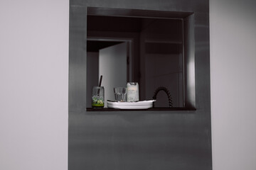 Sleek, minimalist kitchen bar features a pass-through window with two cold drinks one with lime and one creamy beverage,placed on a white tray. 