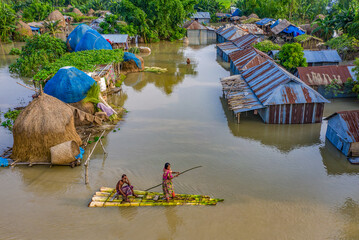 Sariakandi, Bangladesh - 15 July 2019: Aerial view of homes submerged, a raft navigates the floodwaters, contrasting the resilience of the community against the backdrop of submerged landscapes.