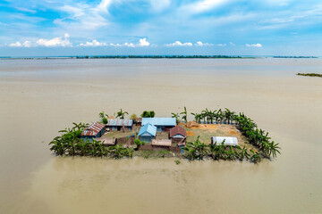Sariakandi, Bangladesh - 15 July 2019: Aerial view of a small, vibrant island community, its structures a testament to resilience amidst the expansive, tranquil waters.