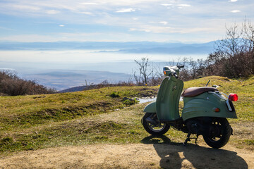 Vintage green scooter rests atop a hill in the Kakheti region of Georgia. The valley is fogged and...