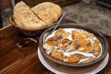 Shkmeruli is a traditional dish originating from the Racha region of Georgia. Chicken is simmered in a creamy garlic sauce. Served with bread on wood table.