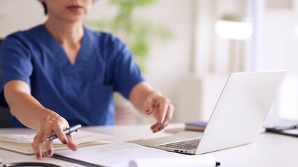 Asian adult female doctor reviewing patient medical records in a modern clinic office setting dedicated healthcare professional studying health information - Powered by Adobe