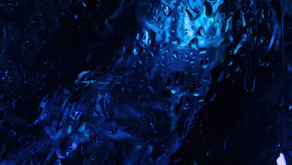 Abstract close-up of wet glass with intense blue neon lighting, water droplets, and smudged...