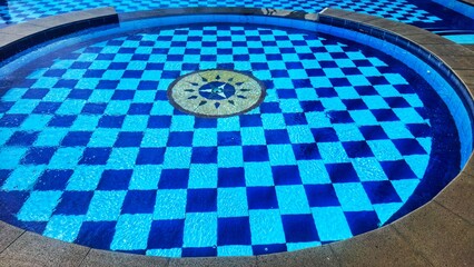 Swimming pool with a checkered floor concept. Medium swimming pool on sunny day with blue sky reflection. Newly installed swimming poolwith with a circular concept and beautiful interior design.