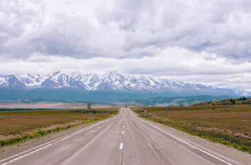 Straight asphalt road in Altai, Russia, stretches into the distance, leading to snow-capped...