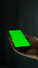 Right hand holding smartphone at slight angle, screen showing green screen, isolated against black...