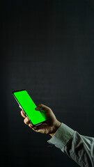Right hand holding smartphone at slight angle, screen showing green screen, isolated against black...