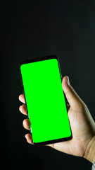Right hand holding smartphone with green screen from front-side angle, dark background, suitable for app display or design template