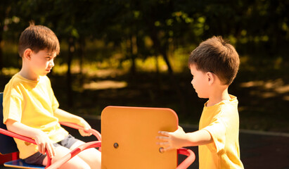 Happy children playing outside in a park on a roundabout with seats. Siblings enjoy a sunny summer...