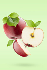 Juicy red apples with green leaves fly as flow on pastel green background, closeup, whole, half and quarter fruit, shadow. Summer fruits for advertising, design, branding, label product.