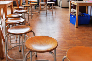 A row of round wooden stools with metal legs placed along a wooden floor in an empty classroom or art studio. Selective focus
