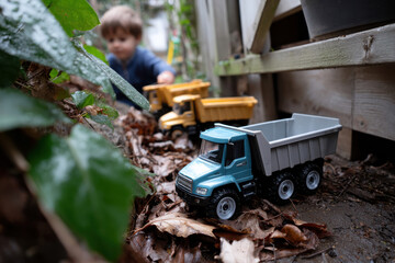Fototapeta premium A child plays with toy trucks in a garden, surrounded by nature and foliage. The scene captures the innocence and joy of childhood exploration and imagination.