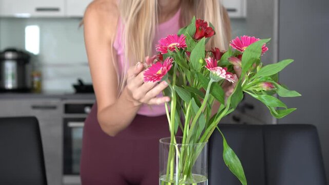 Smiling woman enjoying scent of gerbera daisies and alstroemeria at home