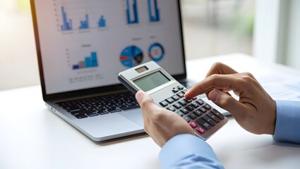 Close up of a person using a calculator while working on a laptop with financial charts