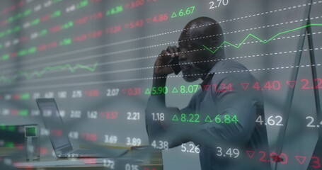 Talking on smartphone, executive viewing laptop at office desk amid floating stock market charts