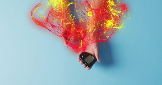 Hand holding black blood glucose meter on light blue tabletop, with red yellow digital waveforms