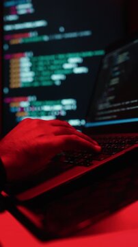 Close-up hand keyboard Hacker in balaclava with an obscured face is stealing data, representing cybercrime, hacking, dark web activity, and online security threats in red light. Cyber Security.
