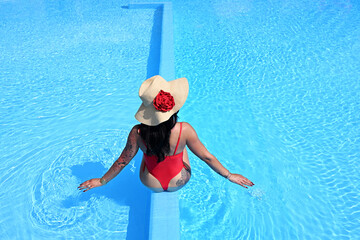 Beautiful woman in a hat and red swimsuit in the pool