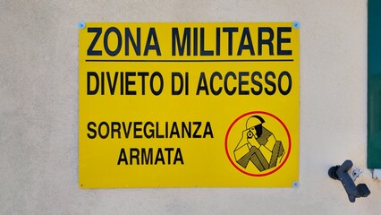 Military zone warning sign with &ldquo;No Entry &ndash; Armed Surveillance&rdquo; message on yellow background, posted on a wall in Italy. Rome, Italy, August 6, 2025