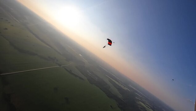 Two skydivers glide gracefully over vast green fields during sunset, capturing the peaceful yet thrilling experience of skydiving at dusk.