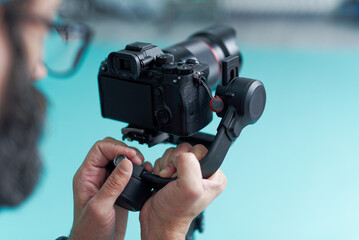 In a modern indoor space, a photographer focuses intently on fine-tuning a gimbal stabilizer while...