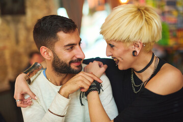 A man and woman share a playful interaction at a neighborhood cafe, smiling and laughing while sitting close together, creating a warm and intimate atmosphere in the late afternoon light