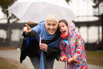 A grandmother and her granddaughter are enjoying a playful moment in the park, pointing out...