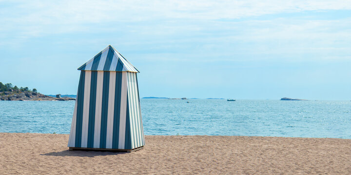 Sunny sandy beach in Hanko, Finland, with colorful iconic changing cabin, hut, booth, a cheerful Finnish Riviera vibe and relaxing seaside summer resort atmosphere with a sea view