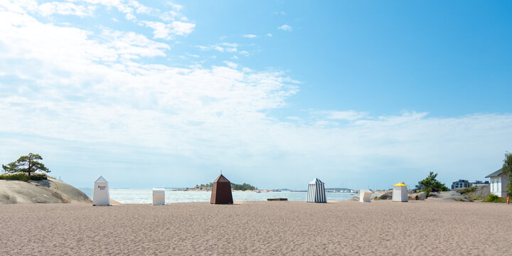 Sunny sandy beach in Hanko, Finland, with colorful iconic changing cabins, huts, booths, a cheerful Finnish Riviera vibe and relaxing seaside summer resort atmosphere with a sea view