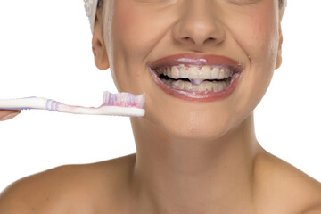 Close-up of woman’s mouth with toothpaste foam on teeth, holding toothbrush, studio shot on white...