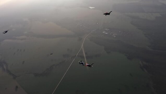 A group of parachutists makes a free fall over vast green fields and rural landscapes, demonstrating the thrill and precision of teamwork in the air.