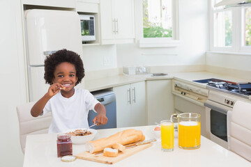 African American child boy sitting at white kitchen table holding spoon and eating cereal from bowl