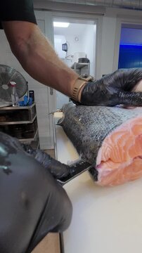 Close-up of chef slicing fresh trout fish with a knife on white cutting board. Professional seafood preparation in commercial kitchen