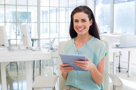 Woman holding tablet in both hands and smiling in open-plan office with white desks and computers - Powered by Adobe