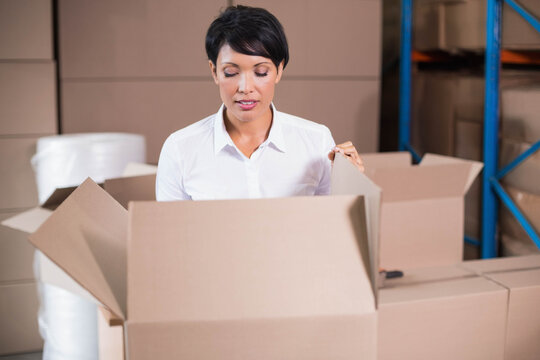 Woman in white shirt opening cardboard box in warehouse storage by bubble wrap and shelving rack