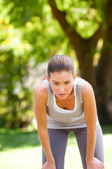 Woman leaning forward with hands on knees in sunlit park wearing gray sportswear pausing workout
