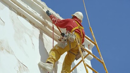 Worker on scaffolding repairs a weathered white building facade - Powered by Adobe