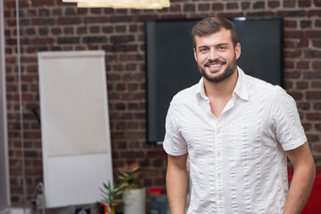 Man in late twenties standing in modern coworking area beside flip chart easel and pendant light