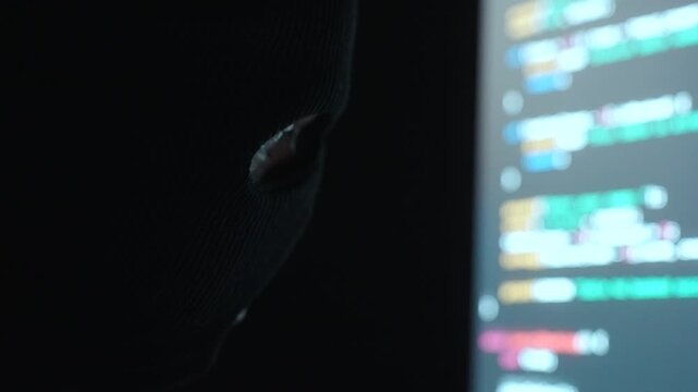 Close-up Thief Hacker in balaclava with an obscured face is stealing data, representing cybercrime, hacking, dark web activity, and online security threats in dark room. Cyber Security concept.
 - Powered by Adobe