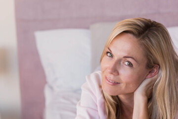 Woman reclining on bed in bedroom with headboard and pillow while smiling toward camera, copy space