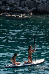 Two cheerful girls enjoying stand up paddleboarding on a sunny day in the sea, ocean, promoting...
