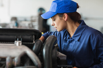 Car engine bay being inspected inside automotive workshop, with hoses, metal parts, and tools