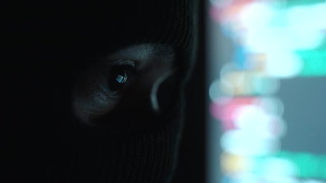 Close-up Thief Hacker in balaclava with an obscured face is stealing data, representing cybercrime, hacking, dark web activity, and online security threats in dark room. Cyber Security concept.
