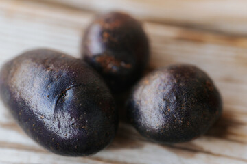 Close-up view of a whole raw purple potato with dark skin placed on a wooden surface in soft...