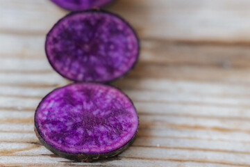 Bright cross-sections of purple potatoes displayed on rustic wooden boards, highlighting their deep color and natural marbling patterns.