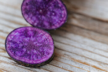 Bright cross-sections of purple potatoes displayed on rustic wooden boards, highlighting their deep color and natural marbling patterns.