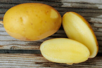 A whole yellow potato and two halves placed on a rustic wooden base, revealing a smooth, creamy...
